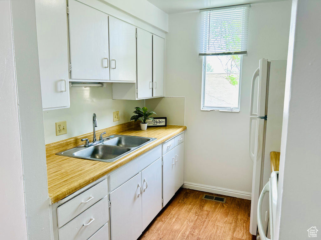Kitchen with a sink, light countertops, light wood-style floors, and white cabinets