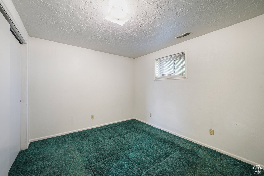 Empty room with dark colored carpet, a textured ceiling, and baseboards