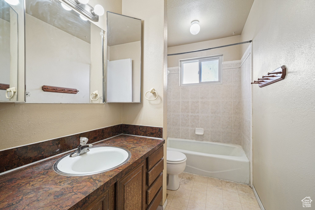 Bathroom featuring toilet, vanity, a textured wall, shower / bath combination, and tile patterned flooring