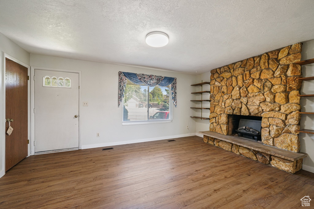 Unfurnished living room with a textured ceiling, wood finished floors, a stone fireplace, and baseboards