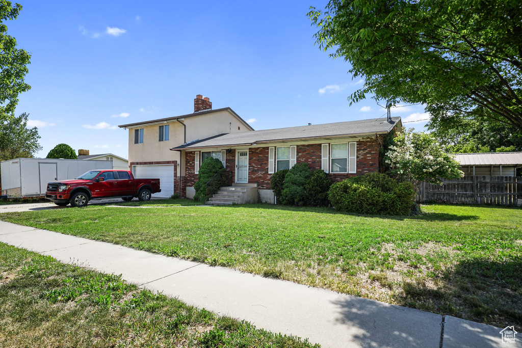 Split level home featuring a chimney, an attached garage, brick siding, and driveway