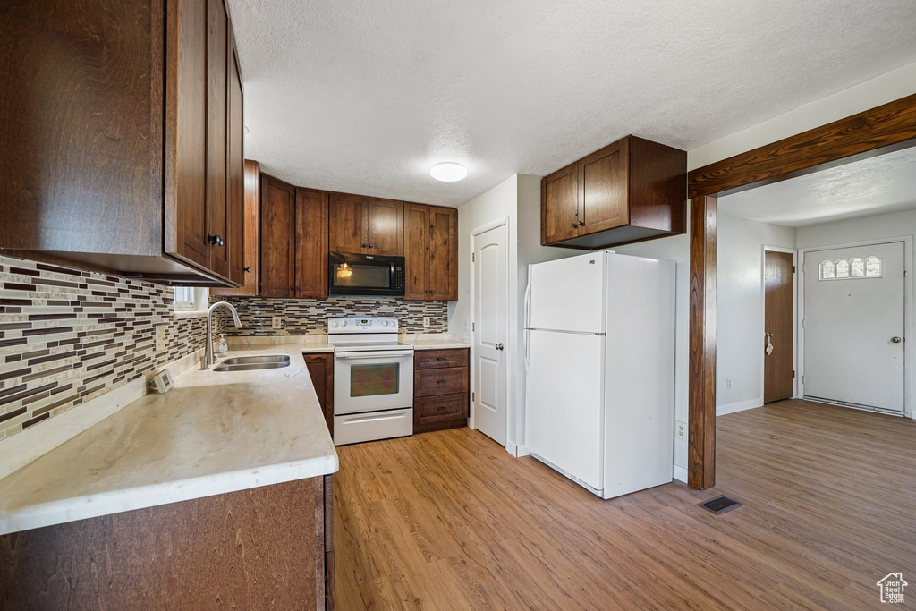 Kitchen with white appliances, a sink, tasteful backsplash, light wood-style flooring, and a textured ceiling