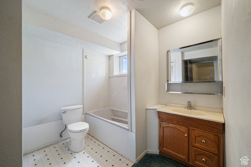 Full bathroom with vanity, toilet,  shower combination, baseboards, and a textured ceiling