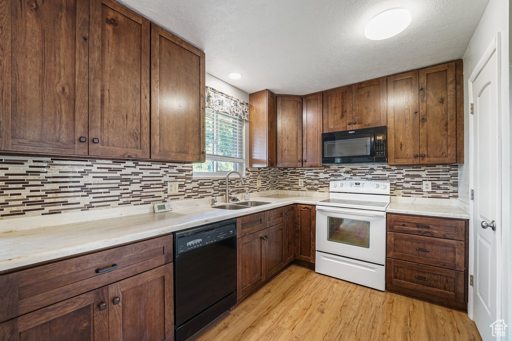 Kitchen with black appliances, a sink, tasteful backsplash, light wood-style floors, and light countertops