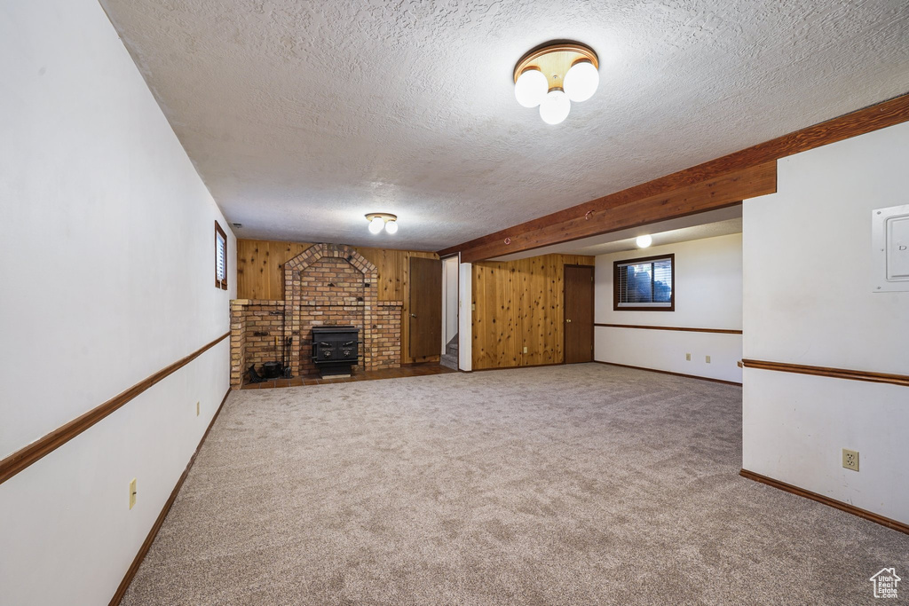 Unfurnished living room featuring a textured ceiling, carpet, baseboards, a wood stove, and plenty of natural light
