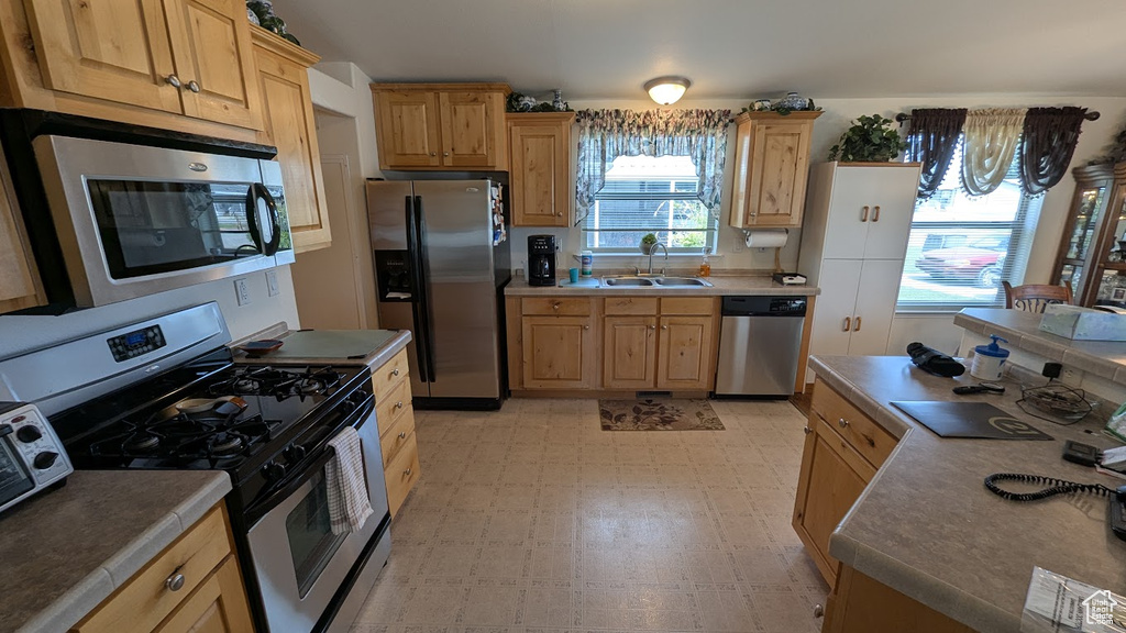 Kitchen featuring stainless steel appliances, light flooring, a sink, and light brown cabinetry