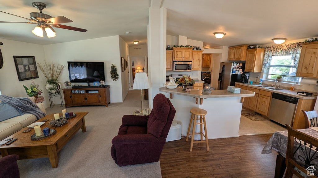 Kitchen featuring open floor plan, appliances with stainless steel finishes, a breakfast bar area, light countertops, and a sink