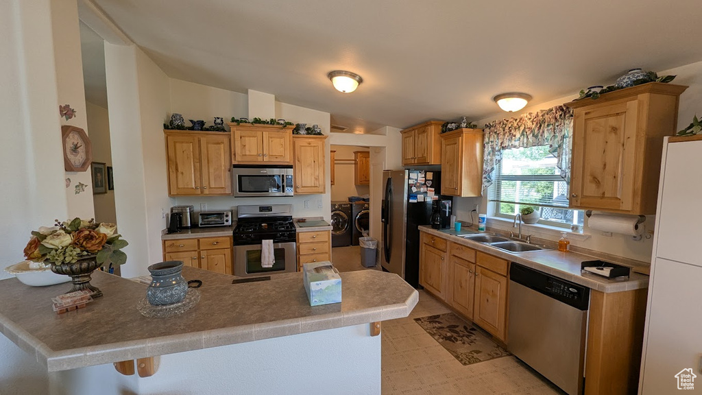 Kitchen featuring stainless steel appliances, independent washer and dryer, a sink, lofted ceiling, and light countertops