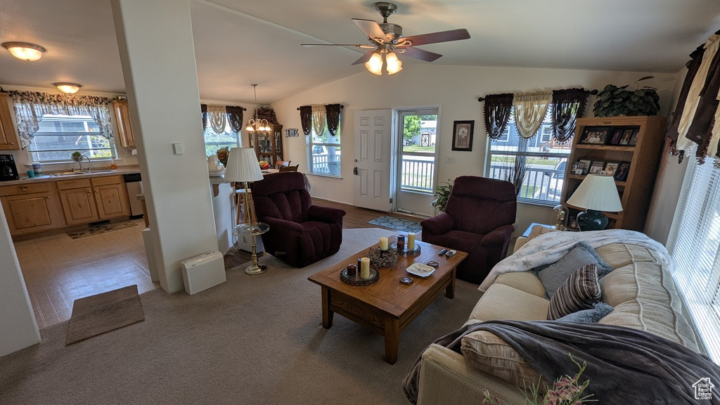 Living room with vaulted ceiling, healthy amount of natural light, a ceiling fan, a chandelier, and light colored carpet