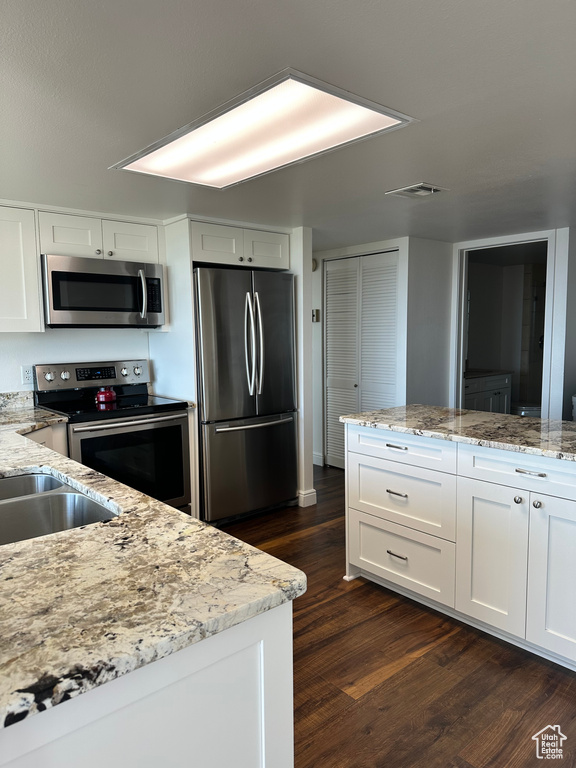 Kitchen featuring stainless steel appliances, white cabinets, dark wood-style flooring, and light stone counters