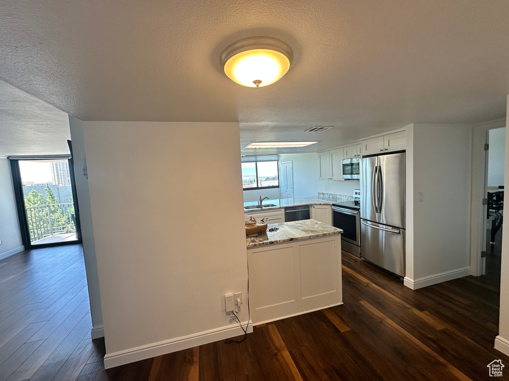 Kitchen with appliances with stainless steel finishes, a peninsula, dark wood-type flooring, light stone counters, and a textured ceiling