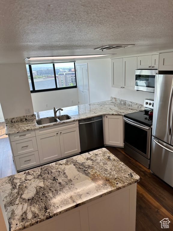 Kitchen with appliances with stainless steel finishes, a textured ceiling, dark wood finished floors, white cabinets, and light stone countertops