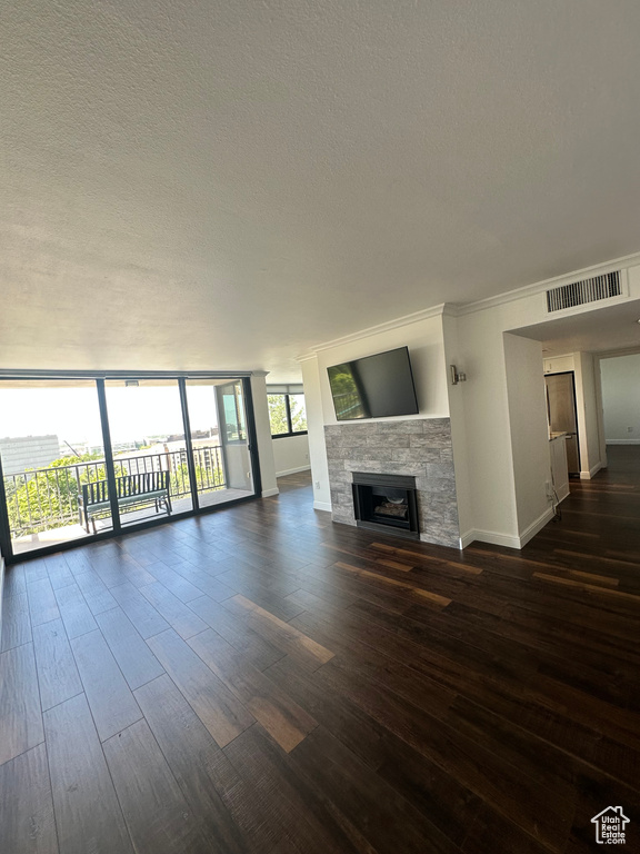 Unfurnished living room with dark wood-style floors, a stone fireplace, a textured ceiling, and crown molding
