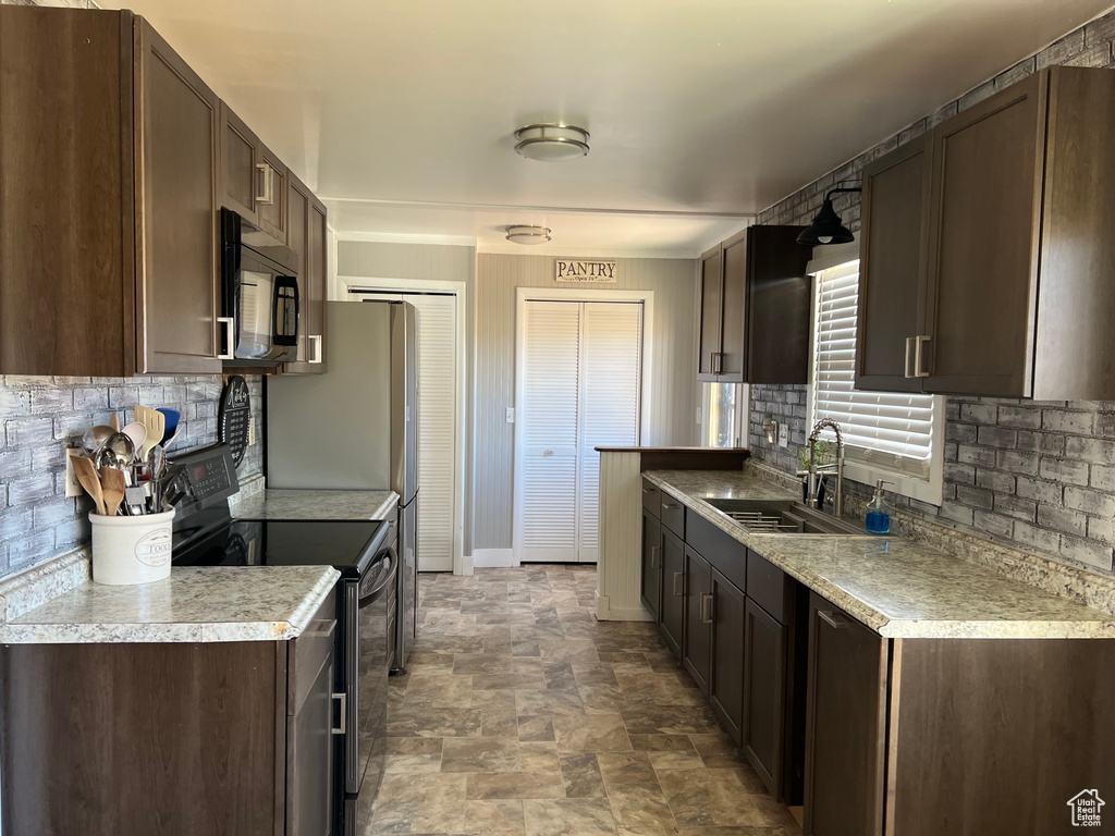 Kitchen with black appliances, a sink, dark brown cabinetry, backsplash, and stone finish floors