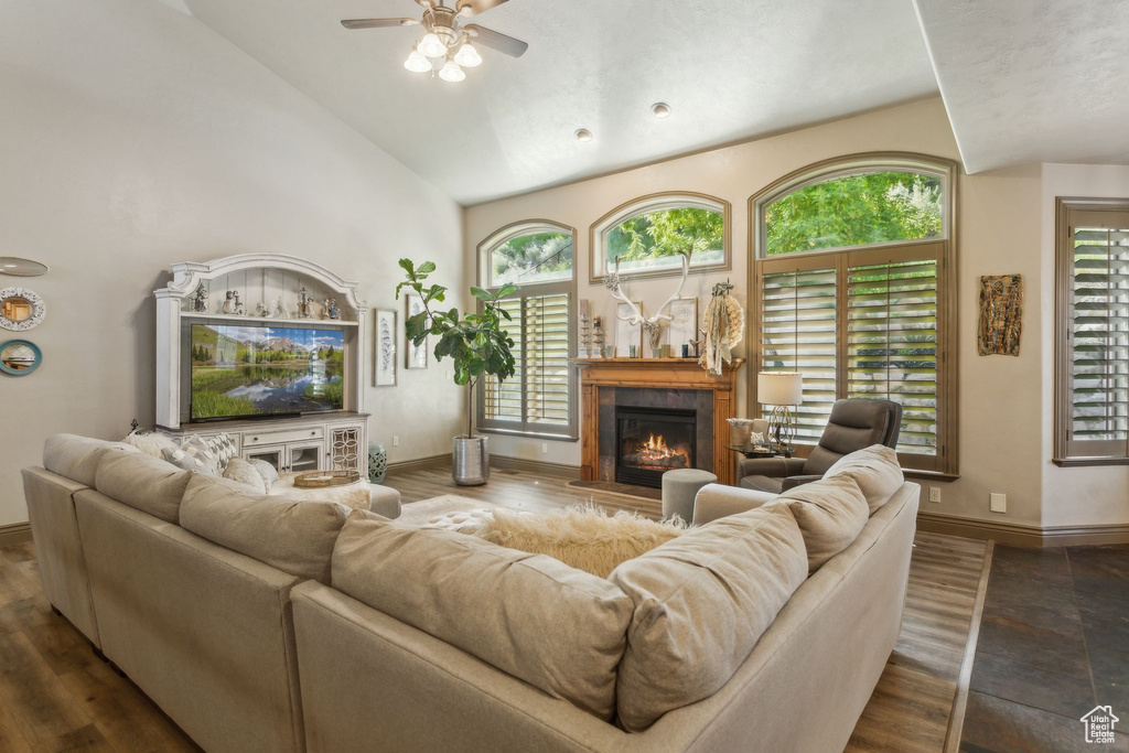 Living area with a ceiling fan, a glass covered fireplace, baseboards, and high vaulted ceiling