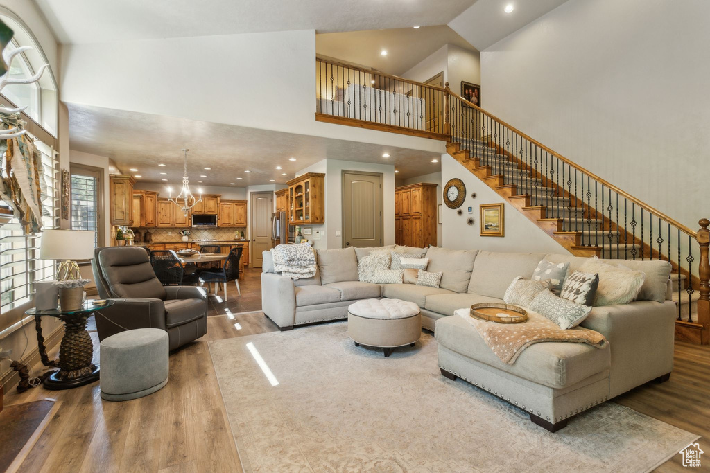 Living room with a towering ceiling, light wood-style floors, a chandelier, stairway, and recessed lighting