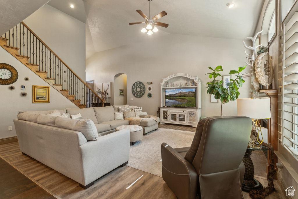 Living room with arched walkways, a ceiling fan, wood finished floors, stairway, and lofted ceiling