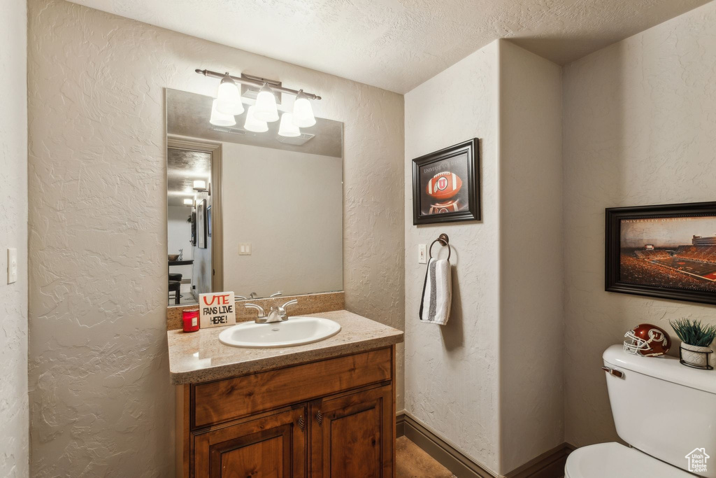 Half bathroom with a textured wall, vanity, toilet, and a textured ceiling