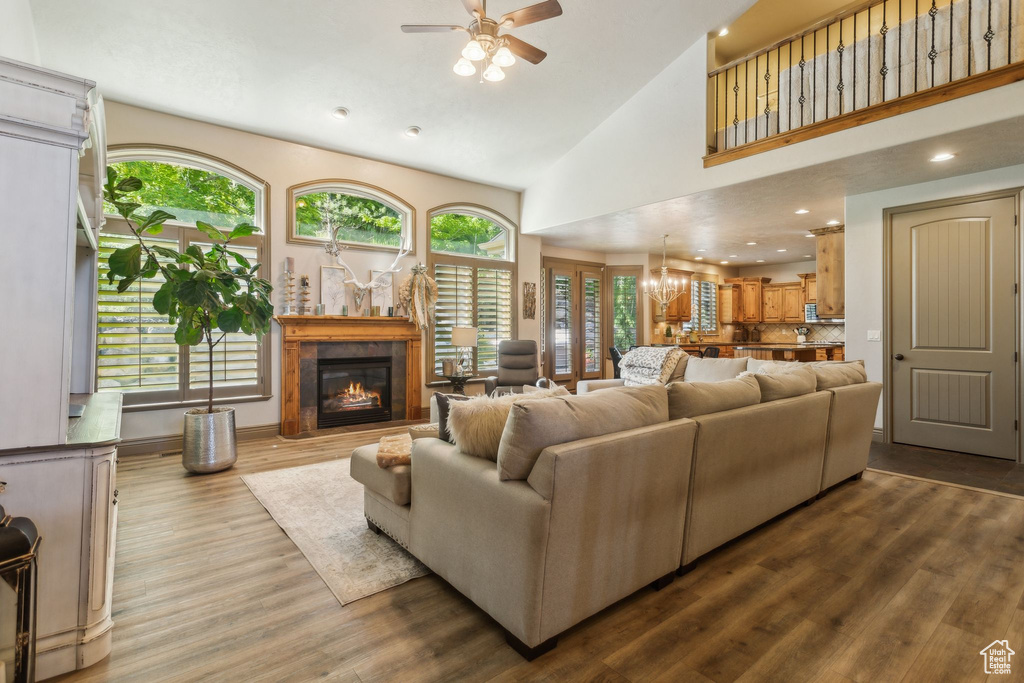 Living area with ceiling fan, healthy amount of natural light, wood finished floors, a glass covered fireplace, and high vaulted ceiling