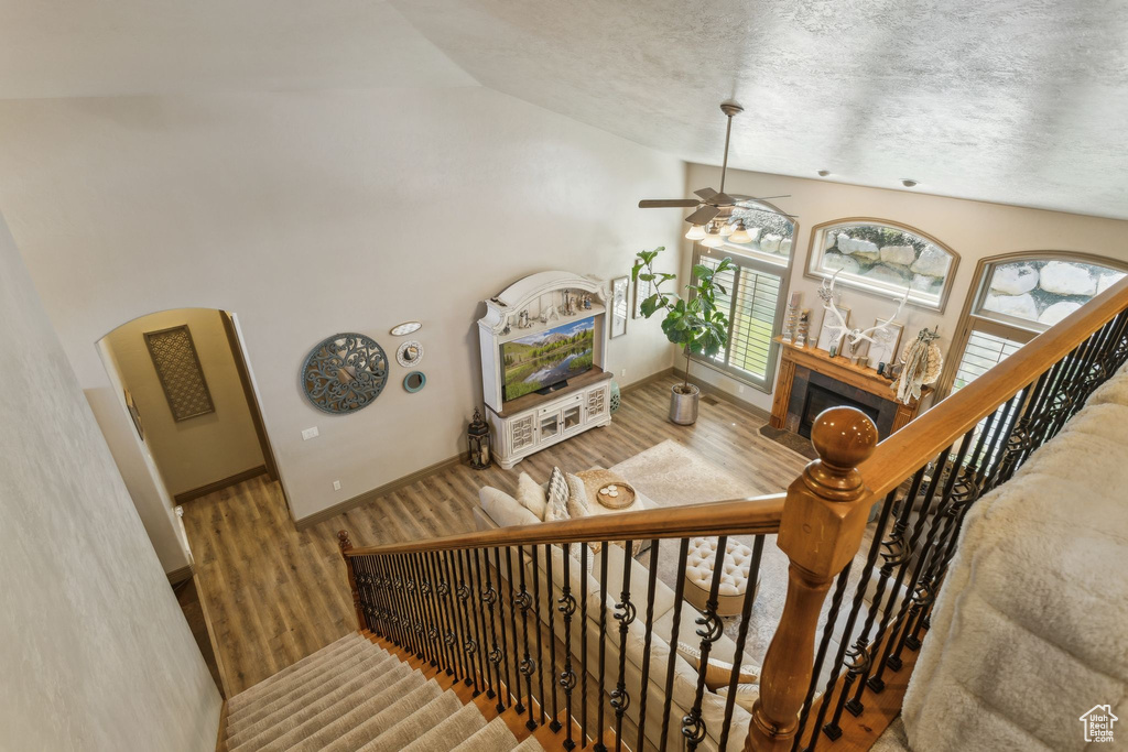 Stairs featuring a ceiling fan, vaulted ceiling, wood finished floors, a textured ceiling, and arched walkways