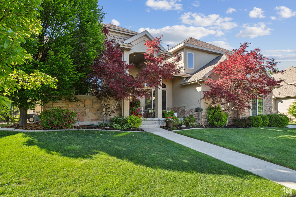 Obstructed view of property featuring stone siding, stucco siding, and a front yard