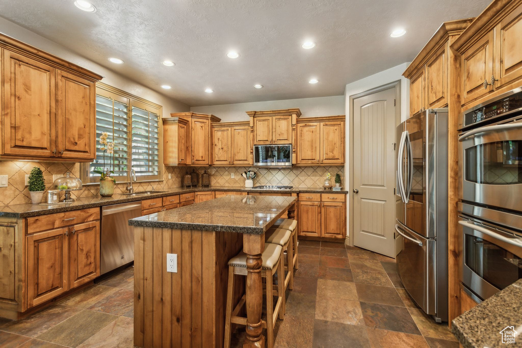 Kitchen featuring stainless steel appliances, stone tile flooring, a sink, a center island, and recessed lighting