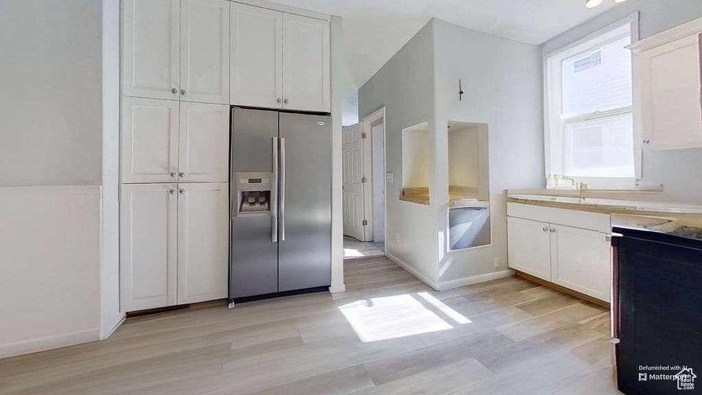 Kitchen featuring stainless steel refrigerator with ice dispenser, white cabinets, light wood-style flooring, and light countertops