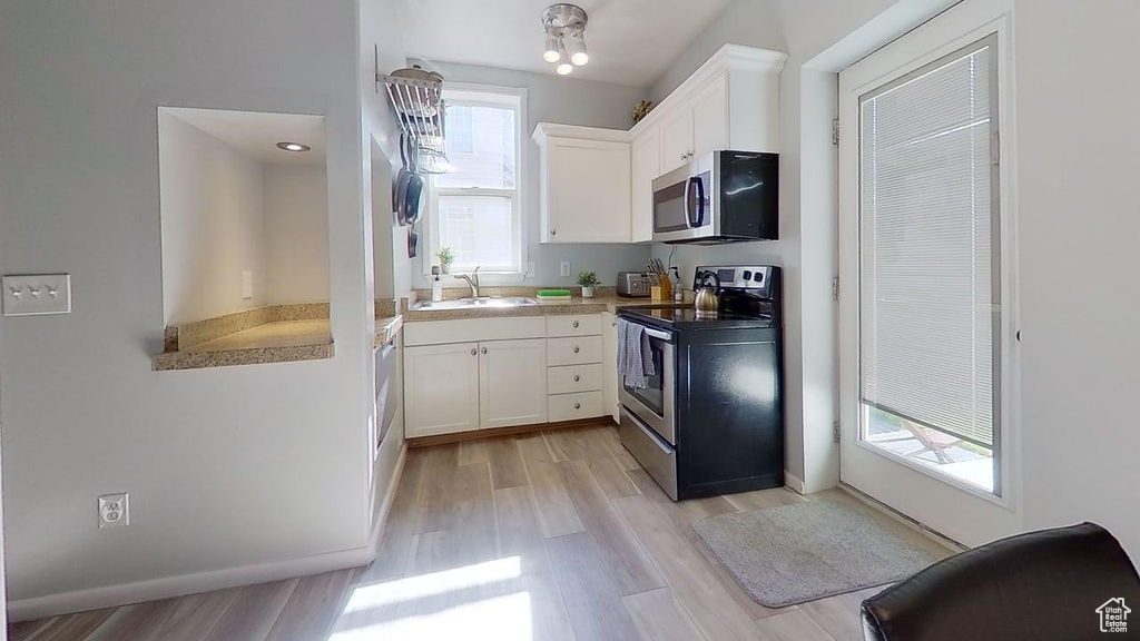 Kitchen featuring stainless steel appliances, white cabinetry, light wood finished floors, and a sink
