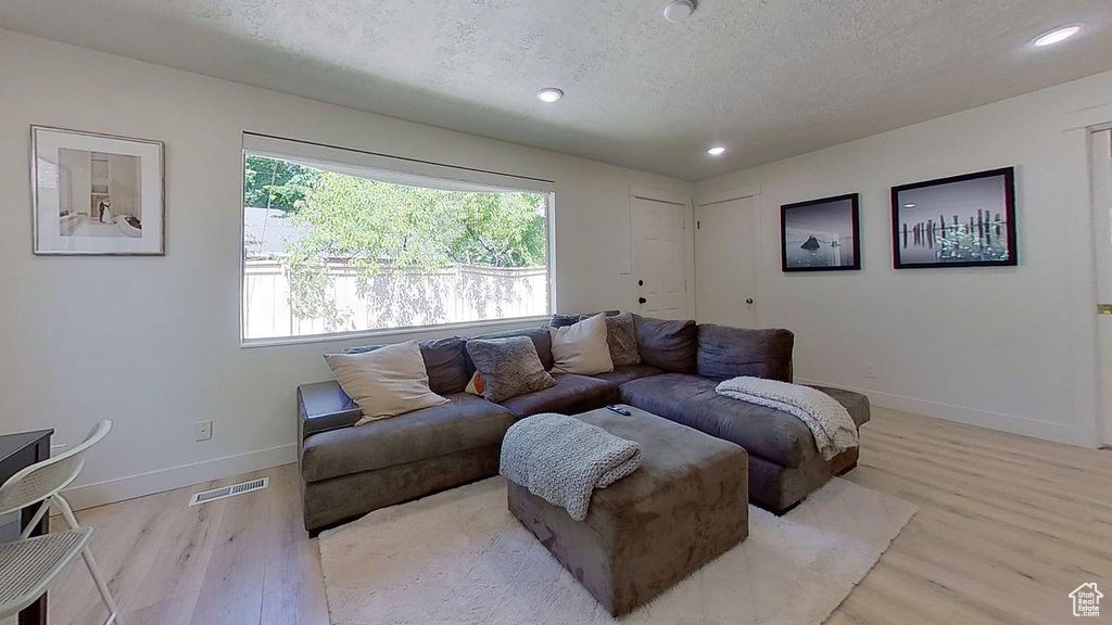 Living area with a textured ceiling, light wood-type flooring, baseboards, and recessed lighting