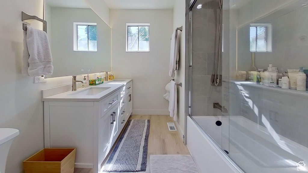 Full bathroom with toilet, vanity, bath / shower combo with glass door, wood finished floors, and baseboards