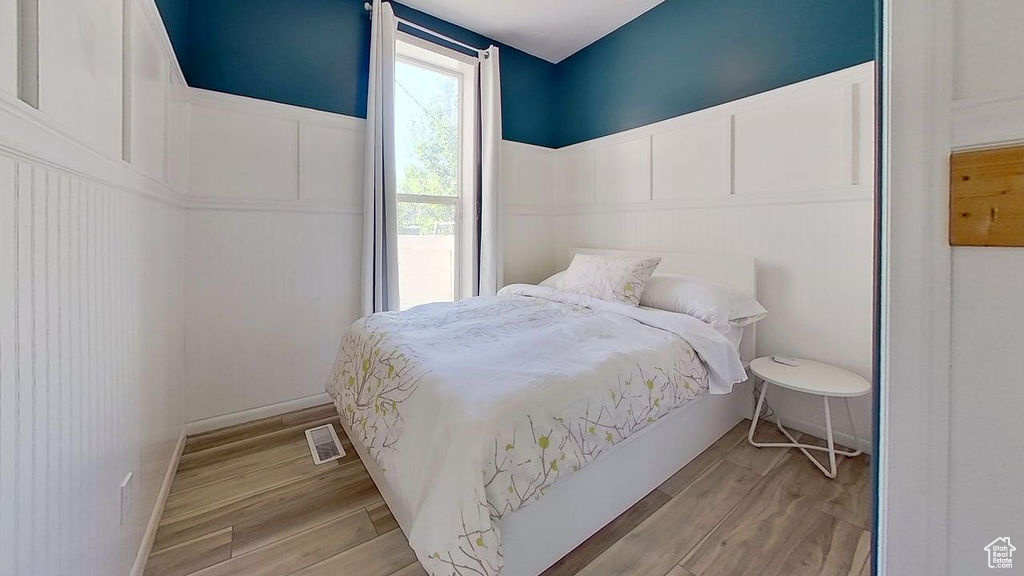 Bedroom with a decorative wall, wood finished floors, and a wainscoted wall