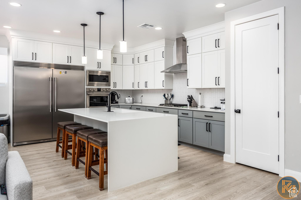 Kitchen featuring built in appliances, wall chimney exhaust hood, a sink, light wood-type flooring, and recessed lighting