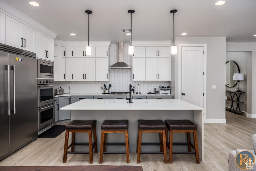 Kitchen with built in appliances, a sink, wall chimney range hood, a breakfast bar area, and tasteful backsplash