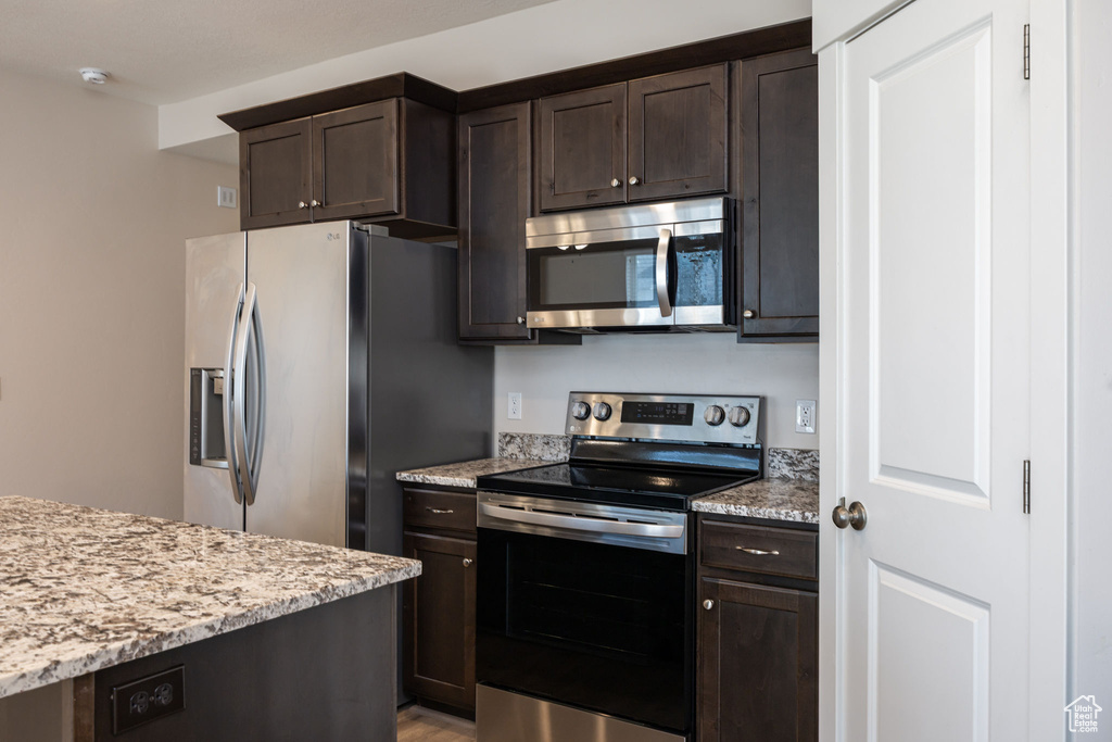 Kitchen with appliances with stainless steel finishes, dark brown cabinets, light stone counters, and light wood-type flooring