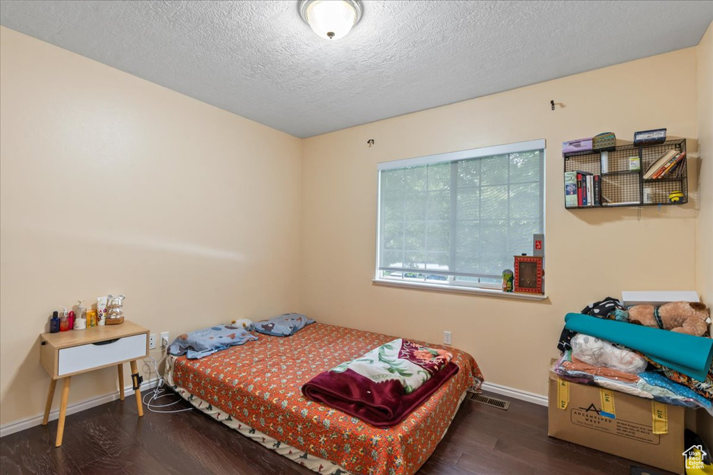 Bedroom with wood finished floors, baseboards, and a textured ceiling