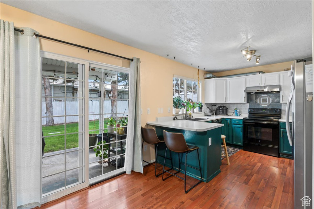 Kitchen featuring electric range, under cabinet range hood, a peninsula, backsplash, and wood finished floors