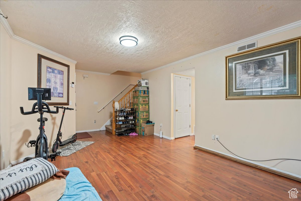 Exercise room featuring a textured ceiling, wood finished floors, ornamental molding, and baseboards