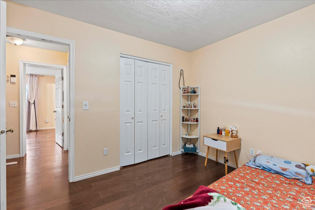 Bedroom with wood finished floors, a textured ceiling, baseboards, and a closet