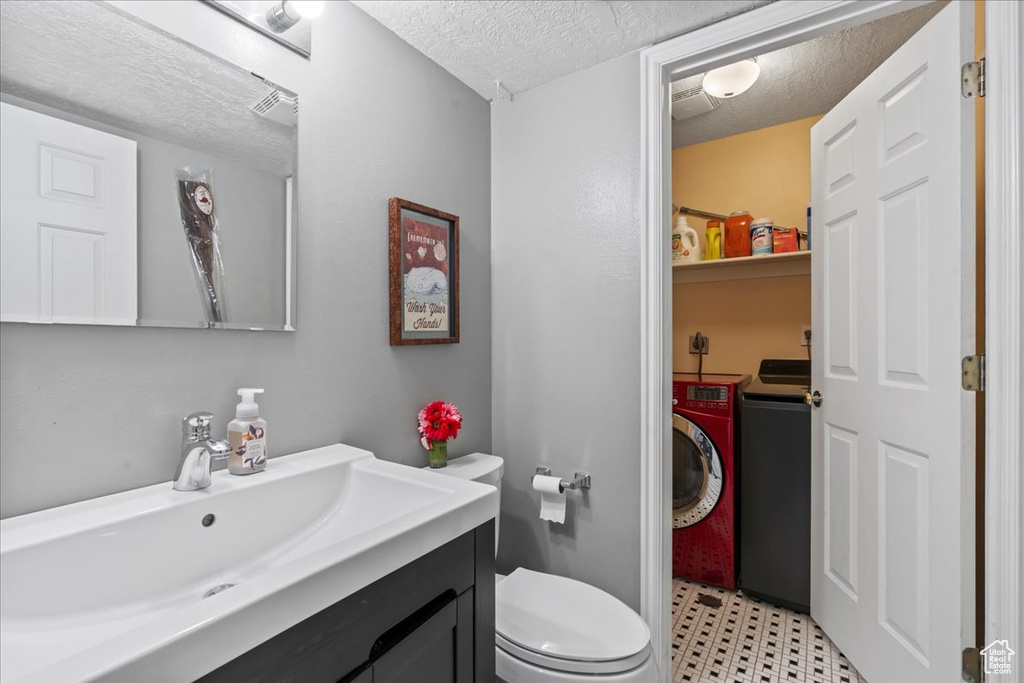 Bathroom with washing machine and clothes dryer, a textured ceiling, toilet, vanity, and tile patterned floors