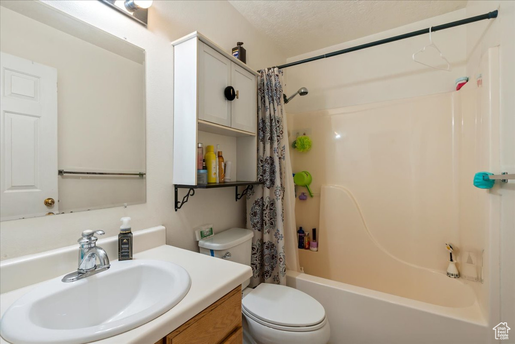 Bathroom featuring toilet, shower / bathtub combination with curtain, and vanity