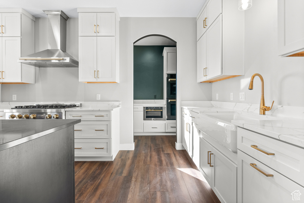 Kitchen featuring wall chimney range hood, dark wood finished floors, a sink, and white cabinets