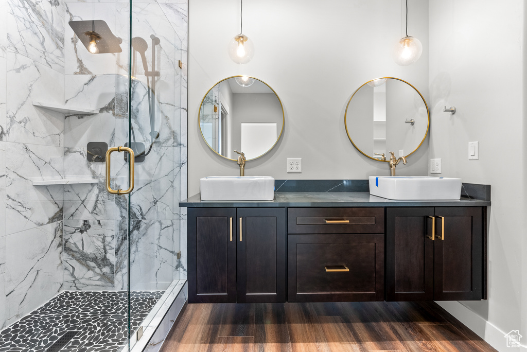Bathroom featuring double vanity, a marble finish shower, wood finished floors, and baseboards