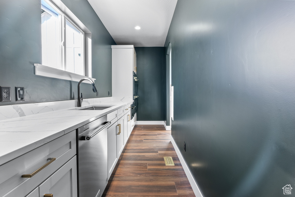 Kitchen with dishwasher, light stone counters, a sink, dark wood-type flooring, and baseboards