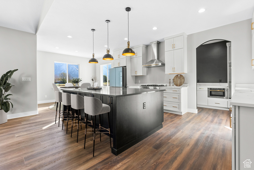 Kitchen featuring wall chimney exhaust hood, freestanding refrigerator, wood finished floors, a kitchen island, and arched walkways