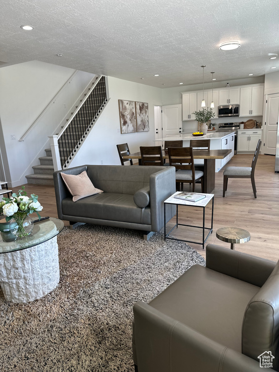 Living area featuring light wood finished floors, stairs, a textured ceiling, and recessed lighting