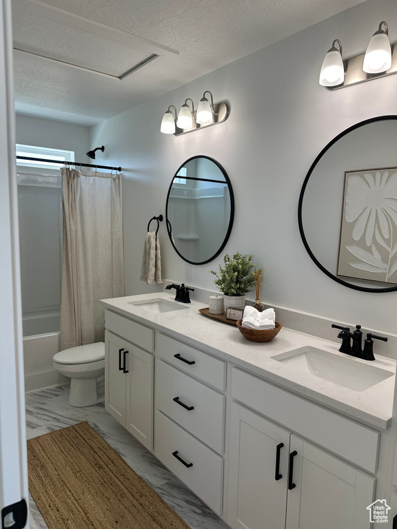 Full bathroom with double vanity, a textured ceiling, toilet, shower / tub combo with curtain, and marble finish flooring
