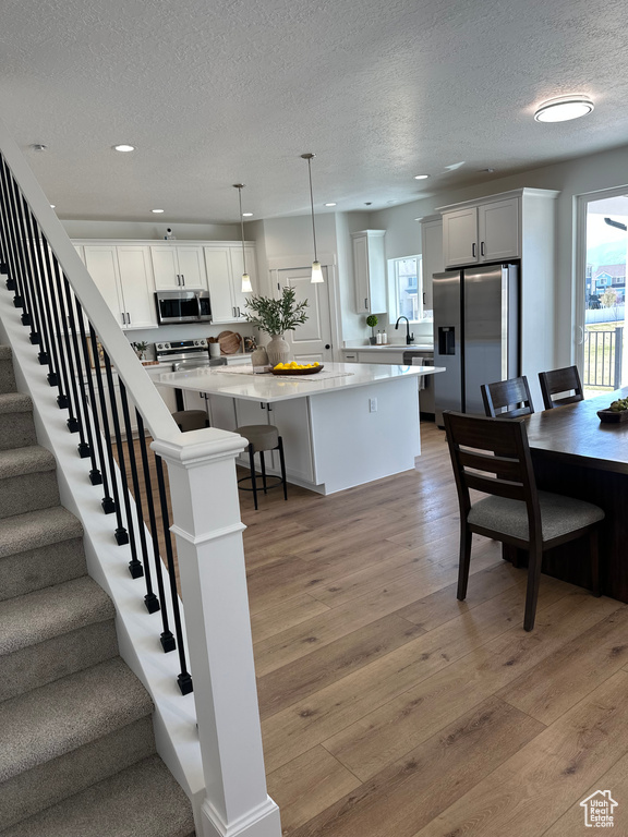 Kitchen with appliances with stainless steel finishes, healthy amount of natural light, a textured ceiling, a kitchen island, and light wood-style floors