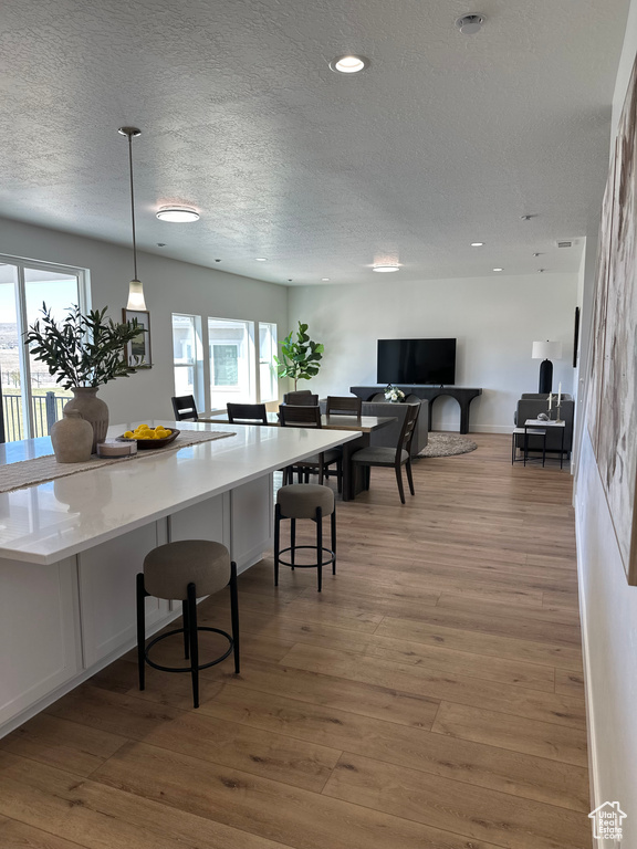 Kitchen featuring a textured ceiling, light wood finished floors, plenty of natural light, decorative light fixtures, and a breakfast bar area