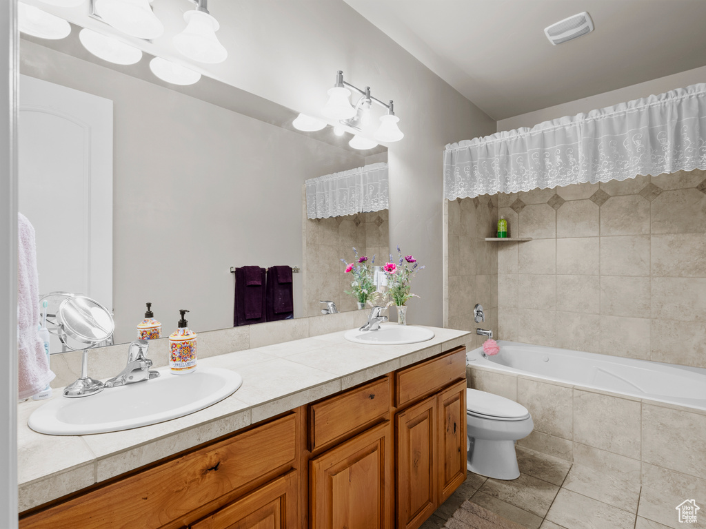 Full bath with double vanity, toilet, tile patterned flooring, and tiled shower / bath combo