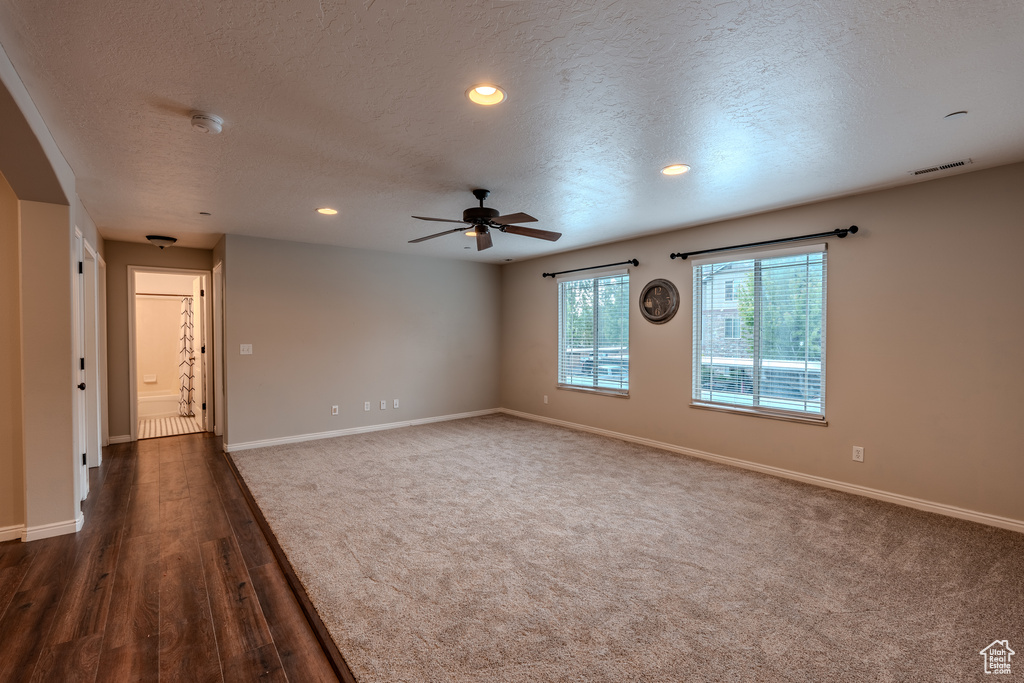 Empty room with a textured ceiling, a ceiling fan, baseboards, a smoke detector, and dark wood-type flooring